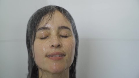 Spa woman showering relaxing under running water in hot shower. Closeup of Caucasian female adult face enjoying relaxation time meditating in warm bath cleaning face and body.
