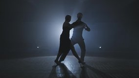 Silhouette of dancers in smoky ballroom. Young couple dance tango in dark room with smoke and spotlights in slow motion. Wide angle in 4K, UHD - Powered by Shutterstock - Get 15% off with code: PIKWIZARD15