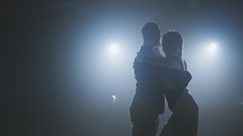 couple performing artistic and emotional dance. Dance element from tango in slow motion. Smoky studio with lights. Medium shot in 4K, UHD