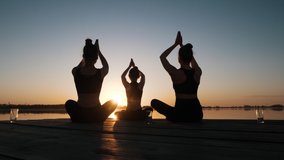 Silhouette of Diverse Group of Three Female Doing Yoga Awe Exercise Sitting in Lotus Position Together on Boardwalk Near Calm Water at Dusks Outdoor. Tranquil Namaste for Emotional Relief, Stress Free - Powered by Shutterstock - Get 15% off with code: PIKWIZARD15