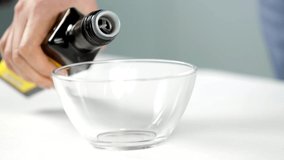 Olive oil pouring from a bottle into a glass bowl. Slow motion.