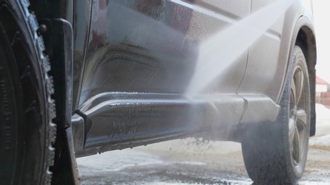Closeup of modern vehicle washed by anonymous person with high pressure water. A very dirty car is cleaned with a jet of clean water