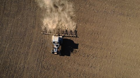 Top view on tractor ploughing dry and dusty farm field and preparing soil for sowing. Drone shot of agricultural work and concept of food industry