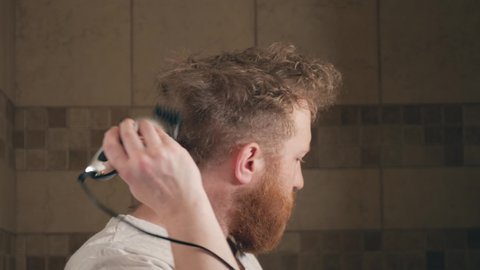 Man using electric clippers to sloppily cut his own hair during the covid-19 lock down.  Adult white male cutting the back of his hair with electric trimmer in bathroom.