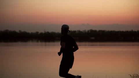 Running Man Silhouette Workout On River Half Marathon.Runner In Sportswear Preparing Triathlon And Workout At Evening.Triathlete Ready For Marathon And Cardio Training Before Running Sport Competition