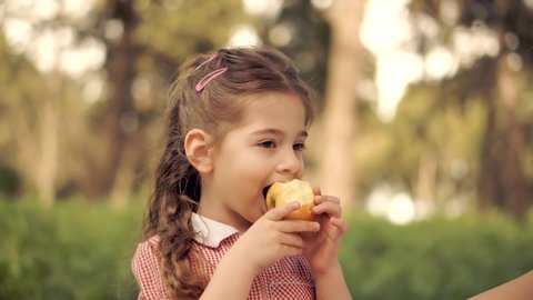 Happy Cute Baby Girl Preschool Eat Fruit In Park. Daughter Kid Eats Healthy Organic And Vegan Food.Little Girl Eating Apple Outdoor. Pretty Child Face.Adorable Carefree Childhood Moment.Cute Baby Girl