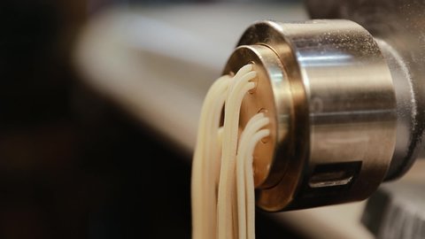 Traditional italian homemade pasta being made on machine for cutting dough. Fresh spaghetti pasta coming out from pasta machine, close-up. Chef uses pasta cutting machine