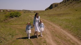 A young mother and her twin daughters, dressed in identical white dresses and denim jackets, walk along a country road on a farm in the spring. Family with twins outside the city in the village. - Powered by Shutterstock - Get 15% off with code: PIKWIZARD15