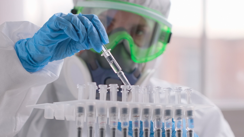 Vaccine vaccination treatment Covid-19 Coronavirus COVID-19 flu virus. Doctor microbiologist virologist researcher scientist in laboratory in PPE, blue gloves analyzing ampoule syringe injection. 4 K | Shutterstock HD Video #1052890007