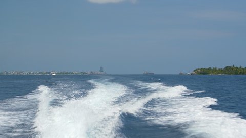 SLOW MOTION: Boat transporting tourists around a group exotic islands leaves a trail of foaming water in the deep blue ocean. Water taxi leaves tropical islands in the Maldives far in the distance.