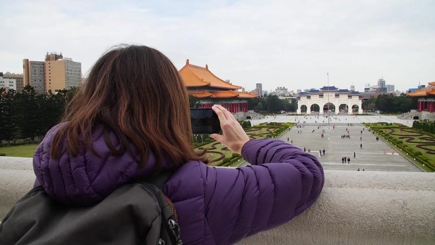 Girl taking a photo with her mobile phone from Chiang Kai Shek Memorial entrance, looking to Liberty Square Arch, theatre and concert hall, Taipei, Taiwan.
Mid angle, traveling movement, slow motion, 