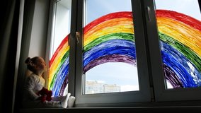 Little girl on background of painting rainbow on window. Kids leisure at home. Positive visual support during quarantine Pandemic Coronavirus Covid-19 at home.  - Powered by Shutterstock - Get 15% off with code: PIKWIZARD15