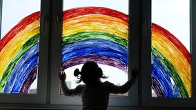 Little girl on background of painting rainbow on window. Kids leisure at home. Positive visual support during quarantine Pandemic Coronavirus Covid-19 at home.  - Powered by Shutterstock - Get 15% off with code: PIKWIZARD15