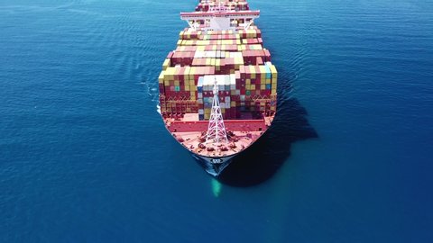 Aerial drone video of Container cargo Ship carrying load in truck-size colourful containers cruising deep blue open ocean sea 