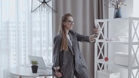 joyful cheerful woman in eyeglasses shooting selfie on front camera using smart phone, sitting in modern workplace and sends an air kiss to subscribers