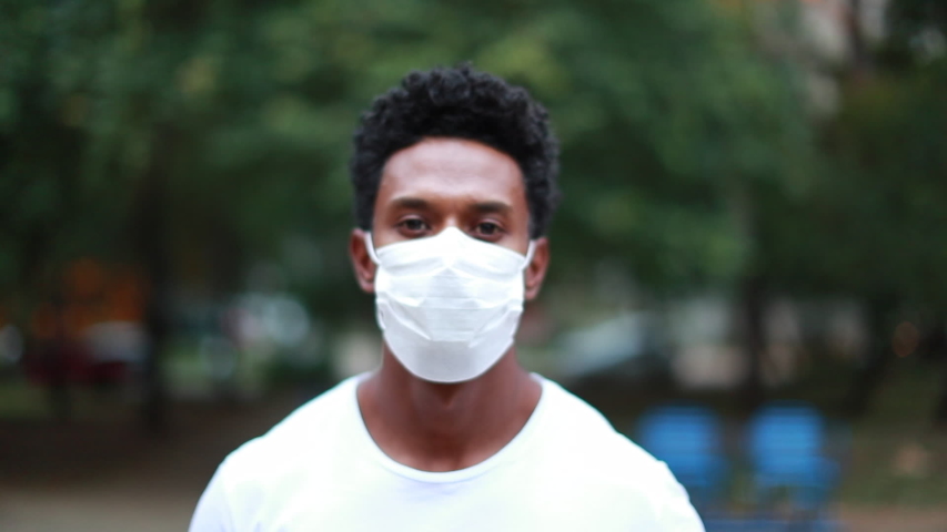 Black african person standing outside at park wearing mask against virus looking to camera Royalty-Free Stock Footage #1052899802