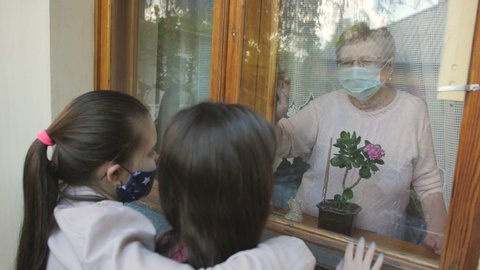 Visit of granddaughters to their grandmother during the coronavirus pandemic. Communication through the window.