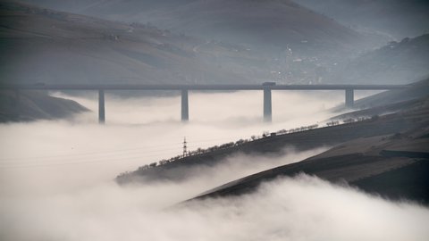 Cinematic 8K 7680x4320.Highway bridge on clouds over.Valley under the bridge is covered with fog and cloud. Vehicles that go fast crossing the road.Vapor aqueous is gaseous phase. Convection traffic.