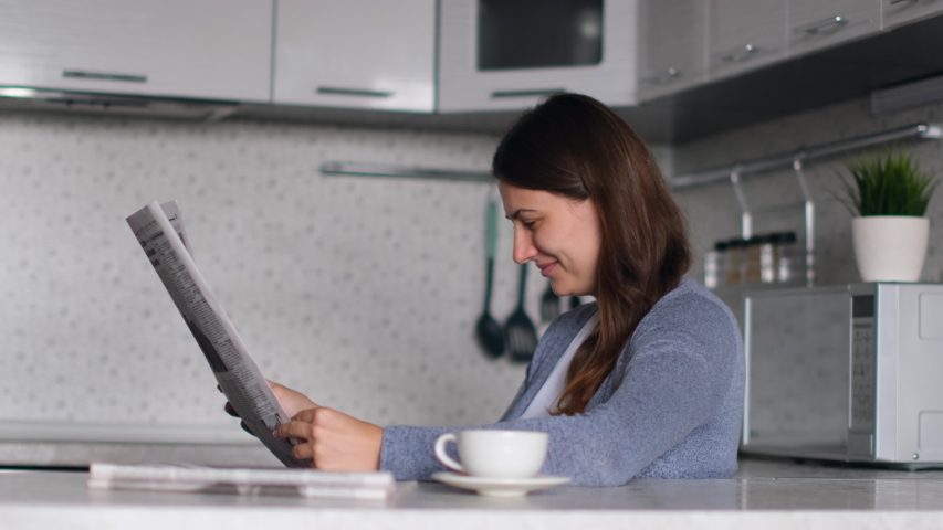 Newspaper News. World pandemic. Source of news. Read newspaper. Attractive female reads a fresh news newspaper while sitting at home in the kitchen. Royalty-Free Stock Footage #1052910347