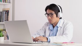 Asian Male Doctor Wear Glasses and Headphone Working with Laptop. Asian male doctor see laptop monitor in serious emotion