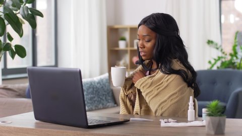 healthcare, technology and people concept - african american sick woman in blanket with tea cup having video call on laptop computer at home
