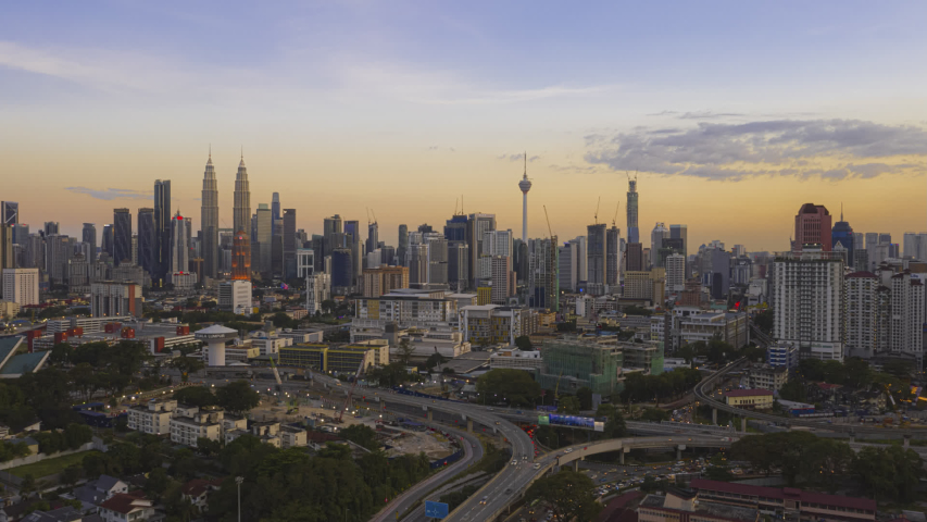 Malaysia Time lapse: Aerial city during dusk overlooking Kuala Lumpur city skyline and the Kuala Lumpur General Hospital with busy roundabout and streets. Pan down motion timelapse. Prores Full HD Royalty-Free Stock Footage #1052913659