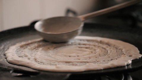 Closeup of making steaming hot 'Dosa' on a cast iron pan. Dosa is the Indian version of pancake made with rice flour dough