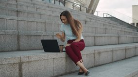 Happy businesswoman using laptop for video call outdoors. Friendly female employee waving hand at webcam on street. Smiling business woman chatting online on computer in modern city