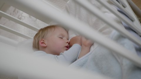 cute little boy sleeps sweetly in his crib and sees colorful dreams in bedroom while sleeping