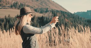 Woman hiker, hiking backpacker traveler camper with her phone camera on the top of mountain in sunny day under sun light. Beautiful mountain landscape view. Hiking, backpacking. 4K slow motion video

