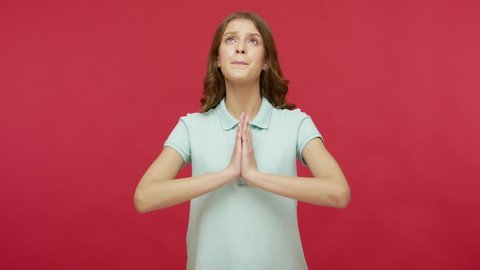 Please, god! Worried, imploring young woman in polo t-shirt sincerely praying and looking up with pleading expression, begging apology, beseeching with hopeful face. indoor studio shot, isolated