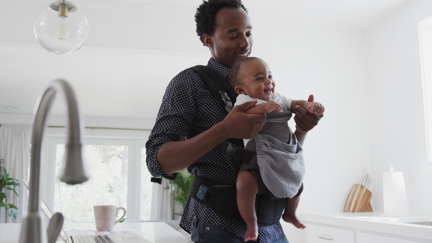 Father with baby son in sling multi-tasking working from home on laptop - shot in slow motion Royalty-Free Stock Footage #1052921768