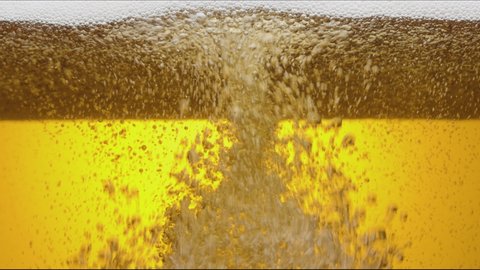 Close-up of the contents of a glass of beer. Beer is slowly poured into a glass, causing a lot of bubbles, waves and foam.