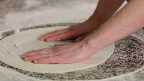 Italian pizza chef forming the dough on a floured surface and kneading it with his hands, in a traditional pizzeria kitchen. Close up