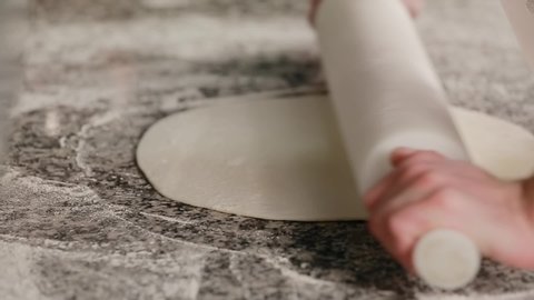 Close up male hands rolls out dough using rolling pin cooking pizzeria. Baker rolling pizza dough on table before baking. Male hands rolling dough on wooden table