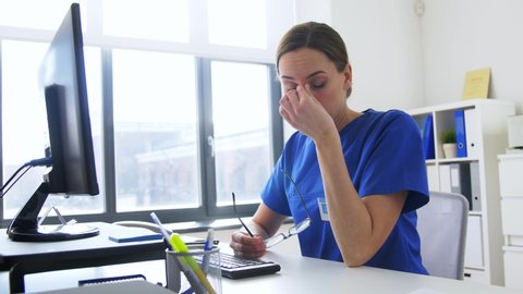 medicine, technology and healthcare concept - tired female doctor or nurse in glasses with computer working at hospital