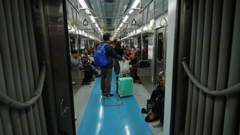 SEOUL, SOUTH KOREA - MARCH 31, 2018: Unidentified Asian man travel by metro, stand with two trolley cases. POV view from passage between cars, rather empty carriage at evening time, some passenger sit