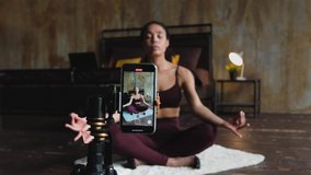 Young attractive african american woman blogger recording video with a smartphone live streaming doing yoga in bedroom at home. Stay at home, quarantine workout concept. Dolly shot