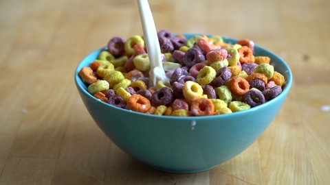 Milk pouring into colourful bowl of cereal, slow motion.