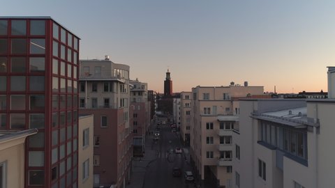 Aerial view of Stockholm street and City Hall building at sunset. Drone shot flying up over street and office buildings, Town Hall tower in the background