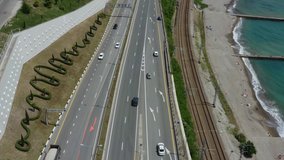 The road along the seashore. Oceanside. Moving forward. Motorway. View from above. Aerial video. Green trees. Clear blue sky. Beach. Sochi. Russia