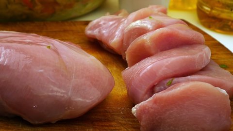 Chicken fillet cut with a knife on a wooden Board.Prepare diet food.White meat without bones.Large pink chunks.Source of protein for athletes.On the kitchen table.Closeup shot.