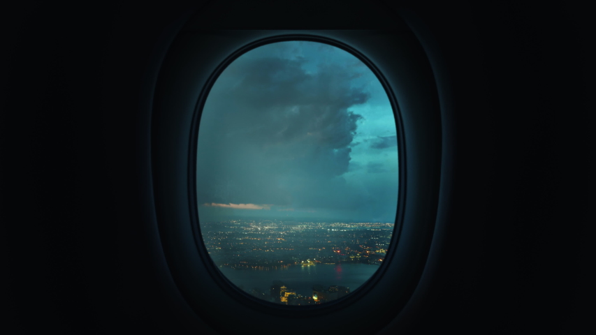 Airplane window view plane flying through storm turbulence with lightning over coastal city | Shutterstock HD Video #1052938277