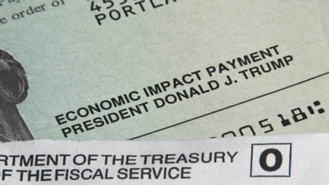 PORTLAND, OREGON / USA - MAY 2020: Person takes "Economic Impact Payment," or Stimulus check, with Donald J Trump's name on it.