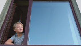 Closeup view video portrait of cute happy healthy white kid looking out from window staying home.