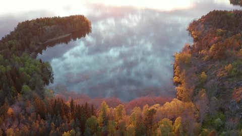 Sunset at lake in aerial drone shot. Beautiful evening light on trees and forest. Water surface mirroring and reflecting colorful clouds in yellow red purple orange. Magical colors evening