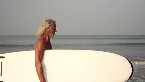 Mature male surfer. Gray-haired old man grandfather on the beach with a surfboard