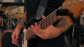 Close-up man hands wearing tattoo professional bassist playing on bass guitar enjoying rock performance drummer playing on drum having live session in music studio