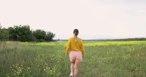 Young woman happy walking through a field and touching yellow flowers. Beautiful carefree woman enjoying nature in blooming field