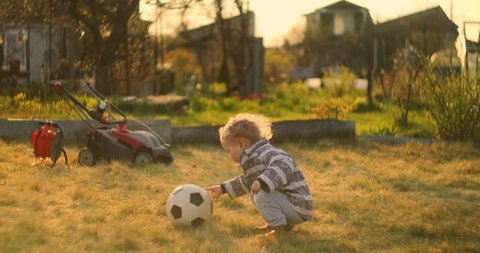 A little boy kicks a soccer ball with his foot in the field behind the house. A little football player in slow motion. Backyard.